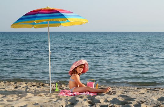happy little girl sitting under sunshade on beach
