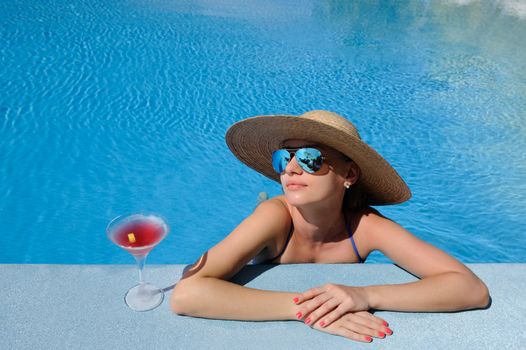 Woman in hat relaxing at the pool with cosmopolitan cocktail