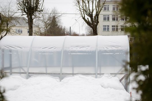 closeup of polythene greenhouse conservatory covered with snow in town house yard in winter season.