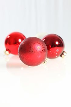 Three colourful red Christmas baubles on a white background with copyspace for your seasonal greetings