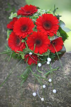 Colourful posy or floral bridal bouquet with vivid red gerbera daisies outdoors on stone with trailing pearls and copyspace