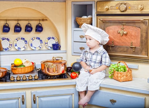 little boy sits on a kitchen table and plays the cook