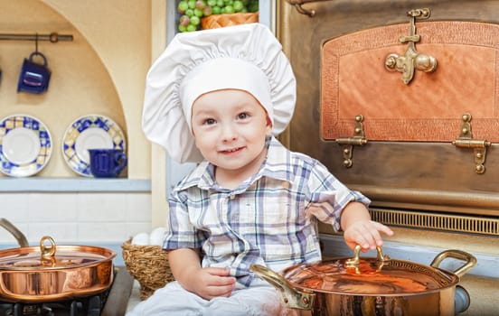 little boy sits on a kitchen table and plays the cook