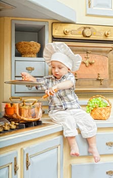 little boy sits on a kitchen table and plays the cook