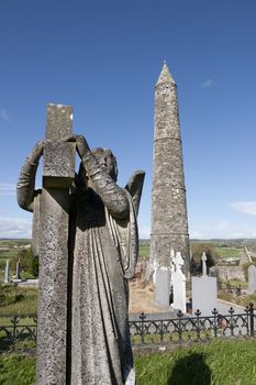 Angel statue before an Ancient round tower and celtic graveyard with cathedral in Ardmore county Waterford, Ireland