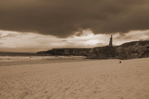 couple meditating on a beach in Ireland with castle in background in sepia
