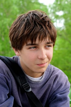 Portrait of the schoolboy sitting on a background of trees