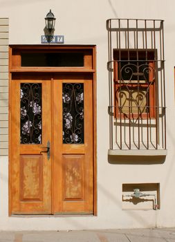 A door with decorative curtains along side a broken window covered with cardboard and wrought iron bars in an urban setting.