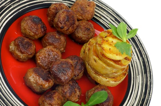 Delicious Roasted Meatballs and Stack of Grilled Potato with Greens closeup on Red Striped Plate