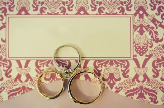 Gold wedding rings and engagement ring on wedding invitation card