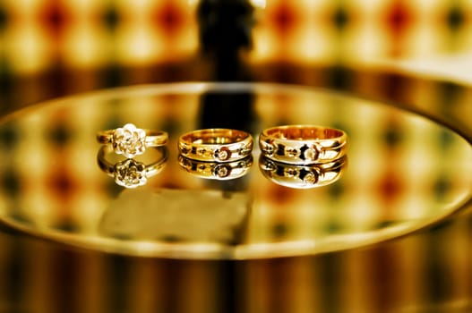 Gold wedding rings with engagement ring on glass table