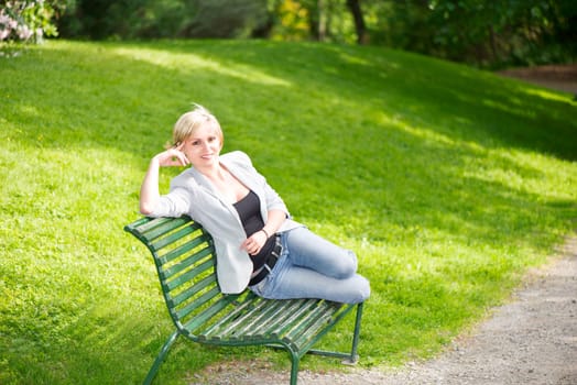 Young woman sitting on bench in park and smiling