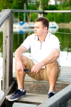 Mature man with sunglasses sitting at pier. Looking away