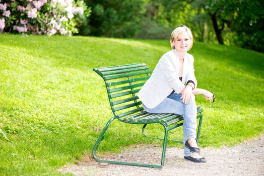 Young woman sitting on bench in park and smiling