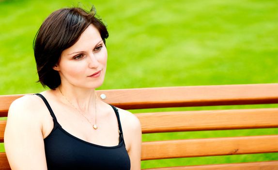Sad brunette woman sitting on a bench against spring green bokeh background