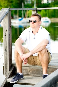 Mature man with sunglasses sitting at pier. Looking away