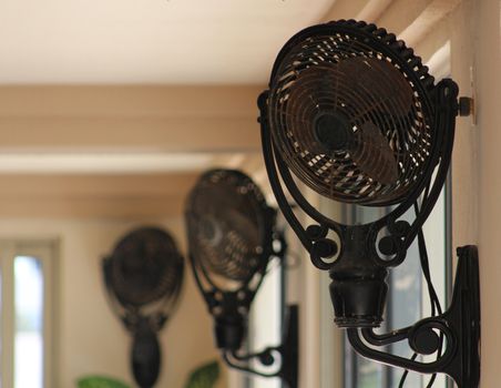 Three vintage fans mounted near the ceiling to provide a breeze in a very large room.