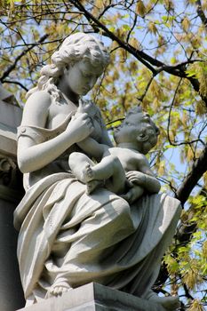 A stone statue of a young woman with a bare shoulder cradling a baby on her lap and holding his hand as he reaches for her face, on a tomb at Graceland Cemetery, Chicago, Illinois, USA