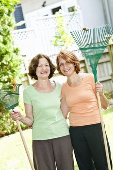 Mother and daughter holding rakes gardening outside