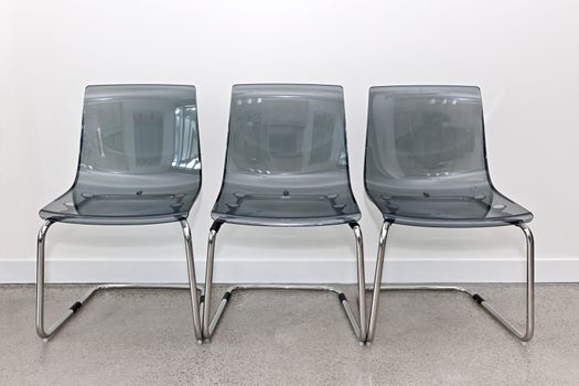 Three gray transparent plastic and metal chairs in a row