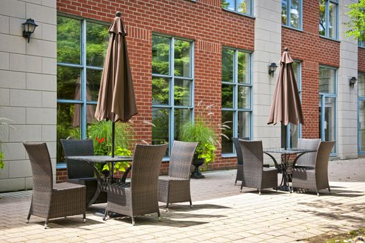 Patio furniture with umbrellas on stone patio near upscale condo building