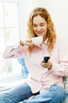 Smiling woman using cordless phone and drinking coffee