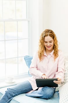 Smiling caucasian woman using tablet computer at home by window