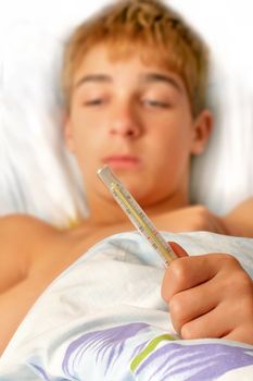 Sick teenager laying in bed with Thermometer