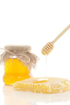 Pot of honey and wooden stick are on a table.