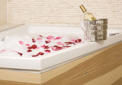 A relaxing bath with rose petals ,wine and glassess