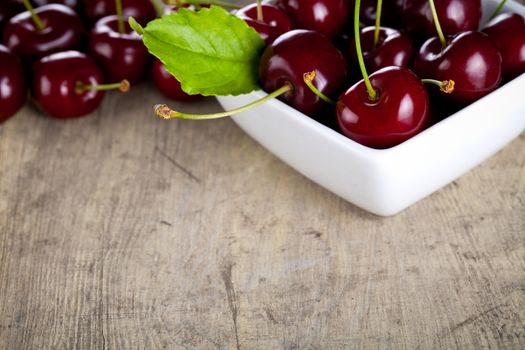 Cherries in white bowl on wooden table background. Copy space. Macro shot