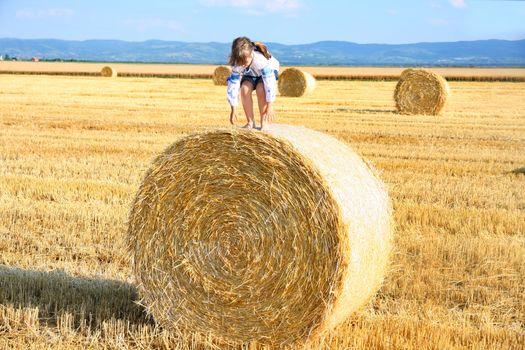 small rural girl on the straw after harvest field with straw bales
