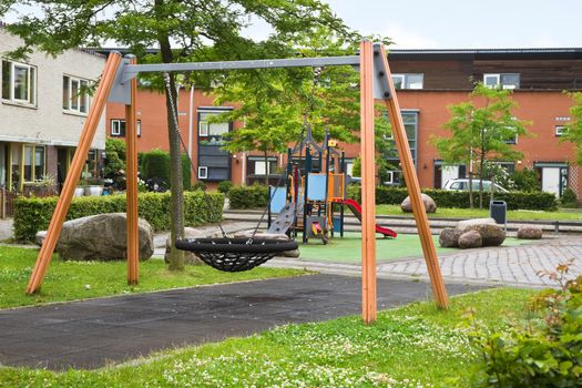 Public playground in modern suburb with colorful wooden climbing construction, swing, slides and rubber floor for safe playing