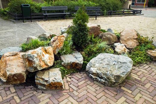 Decorative rock-garden in city street with benches in background as resting place