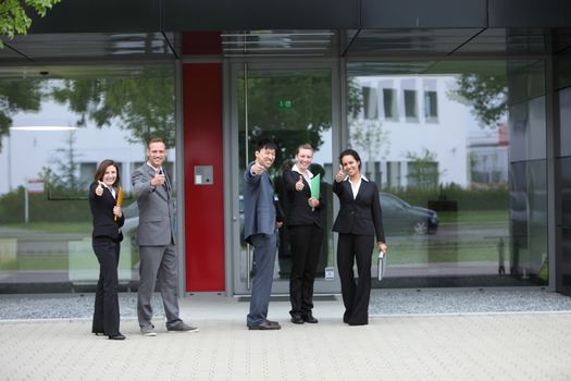 International team of successful business people showing thumbs up in front of a modern building