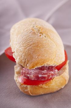 A sandwich with sausage and tomato over brown napkin