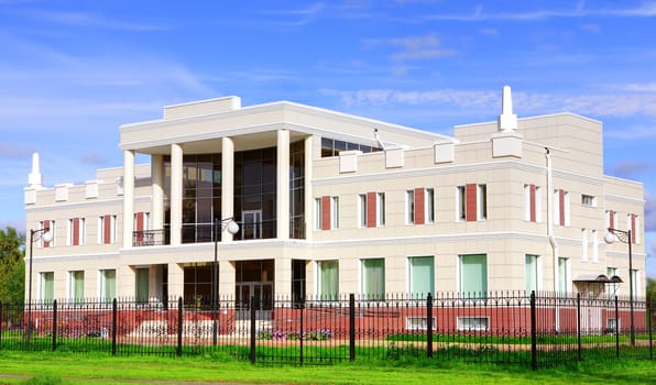 The white two-story building with columns, lined with tiles. White house behind a black metal fence with spikes. The building with a ventilated facade.