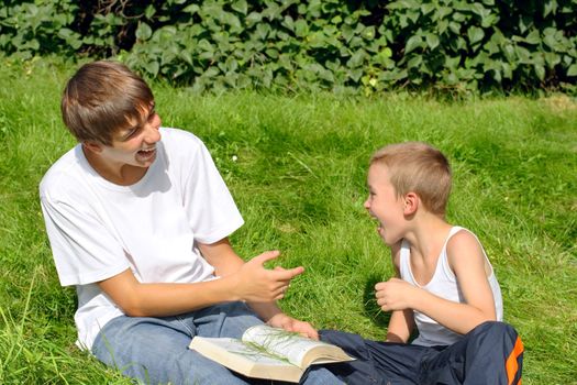 The happy teenager and kid with a book on a summer meadow