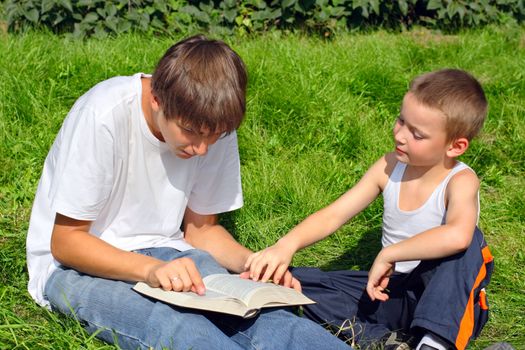 teenager and kid with a book on a summer meadow