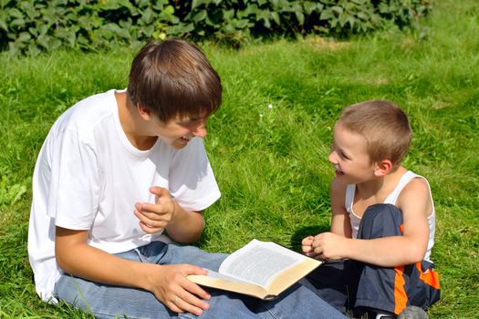 The happy teenager and kid with a book on a summer meadow