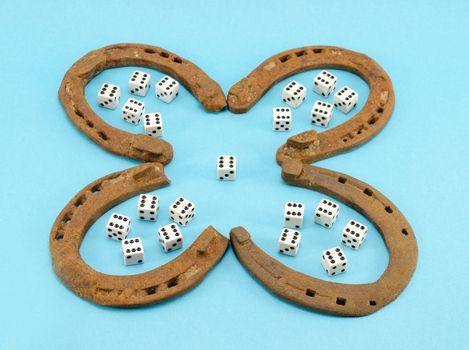 concept of four leaf clover made of rusty retro horse shoes and six number gamble dices on blue background. luck talisman.