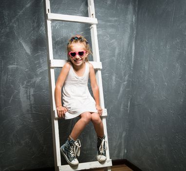 Cute little girl in sunglasses on the white stairs