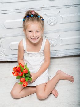 Cute little girl with a bouquet of flowers sitting on the floor