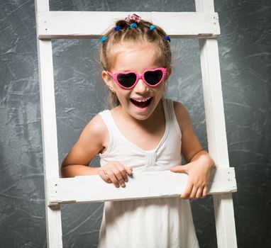 Smiling little girl in sunglasses on the white stairs