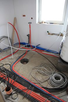 Electrical installation inside a building with an array of pipes and wiring on the floor of the room awaiting the return of the contractors