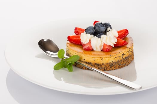 Cheese-cake with strawberries, blueberries, mint and cream on white plate.