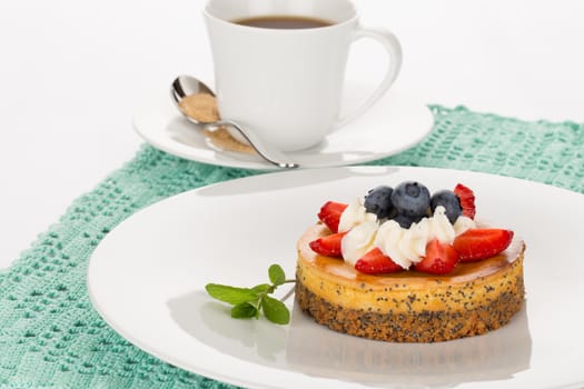 Cheesecake with strawberry, blueberry, mint and cream on white plate with cup of tea.