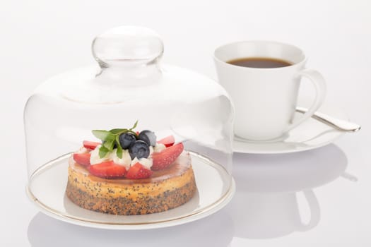 Cheesecake with strawberry, blueberry, mint and cream under glass bell and cup of coffee.