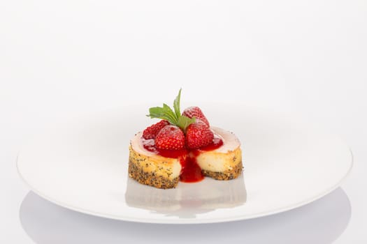 Cheesecake with strawberry, red coulis and mint on white plate.