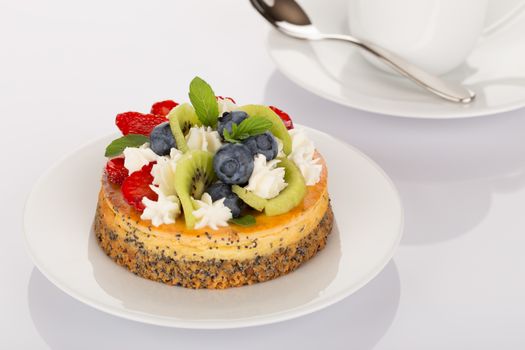 Cheesecake with strawberries, blueberries, kiwi and cream on white plate.